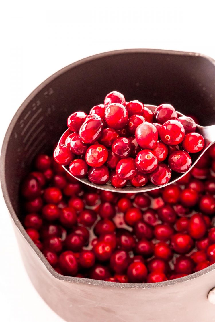 A spoon lifting cranberries out of a pot.