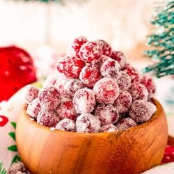 Close up photo of sugared cranberries in a wooden bowl surrounded by holiday decorations.