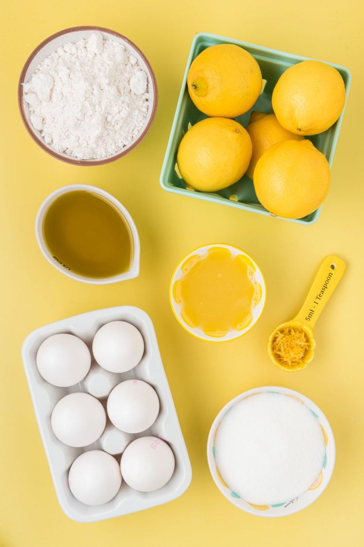Ingredients to make lemon olive oil cake on a yellow surface.