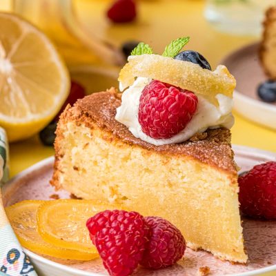 A slice of lemon olive oil cake on a pink plate on a yellow surface.