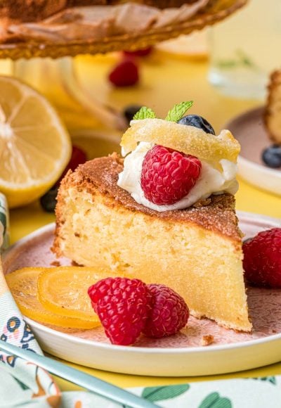 A slice of lemon olive oil cake on a pink plate on a yellow surface.