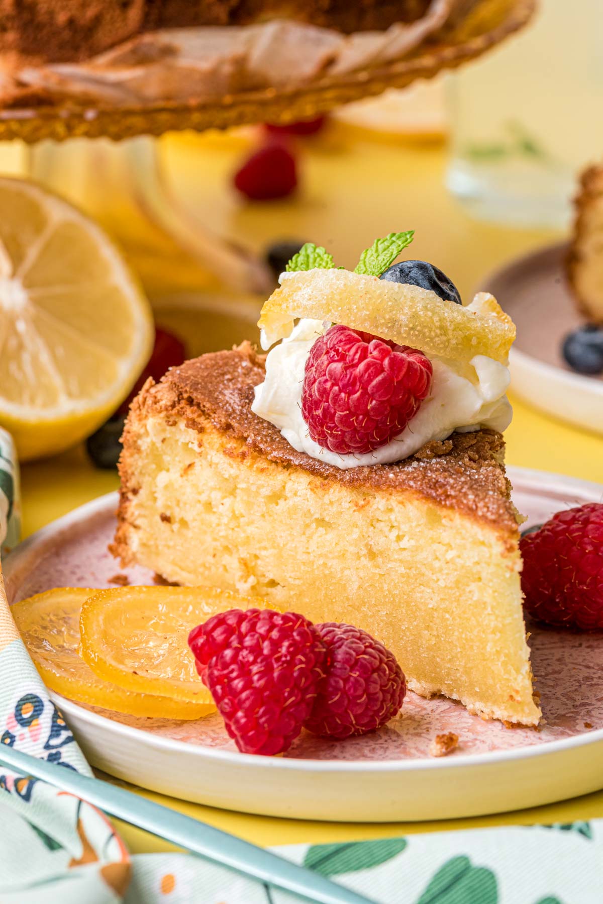 A slice of lemon olive oil cake on a pink plate on a yellow surface.