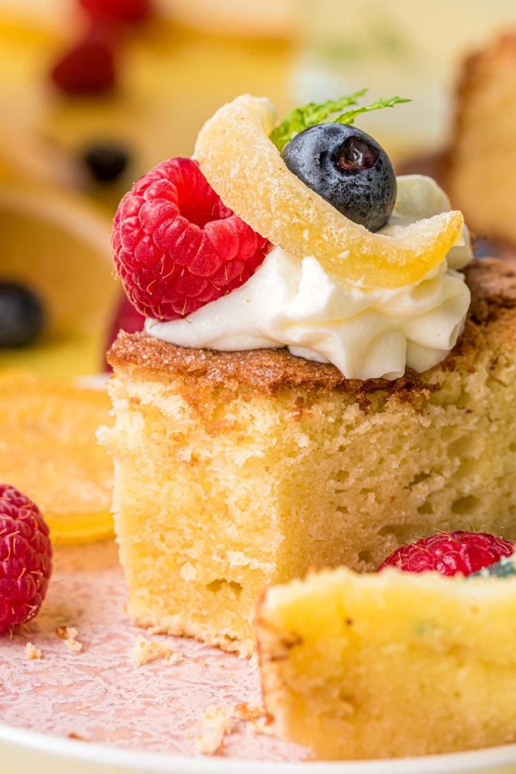 A slice of lemon olive oil cake on a plate topped with cream and berries.