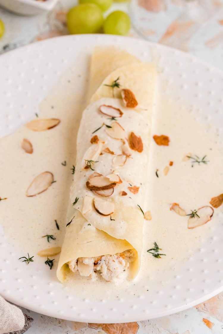 A spinach and chicken crepe topped with a white wine cream sauce and sliced almonds on a white plate.