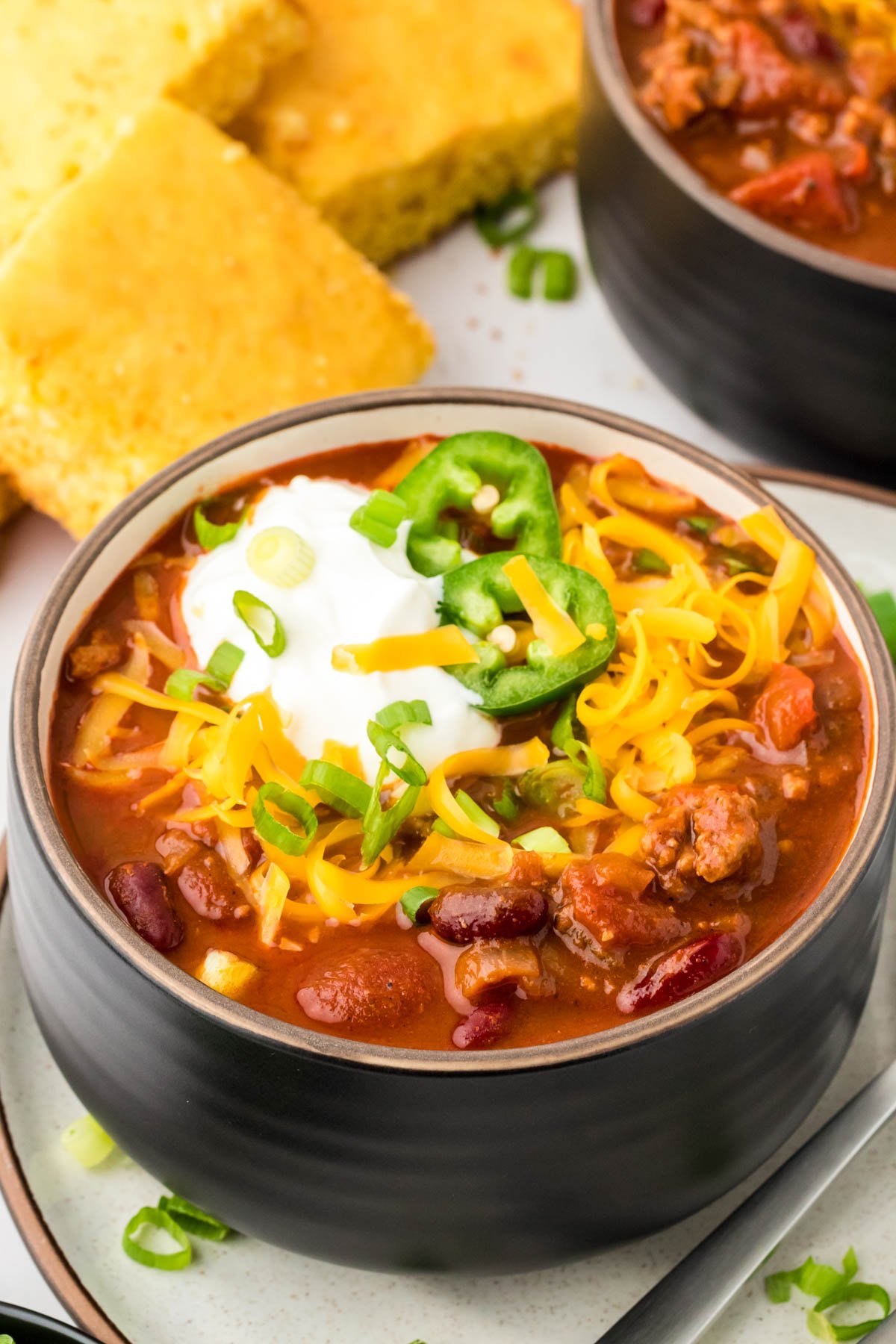 A black bowl filled with turkey chili and topped with sour cream and cheddar.