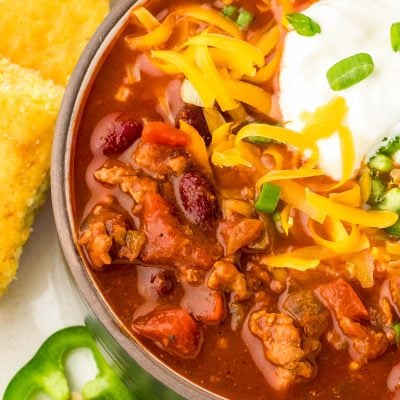 Close up of a black bowl filled with turkey chili and topped with cheddar cheese and sour cream.