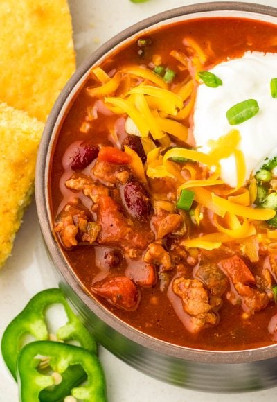 Close up of a black bowl filled with turkey chili and topped with cheddar cheese and sour cream.