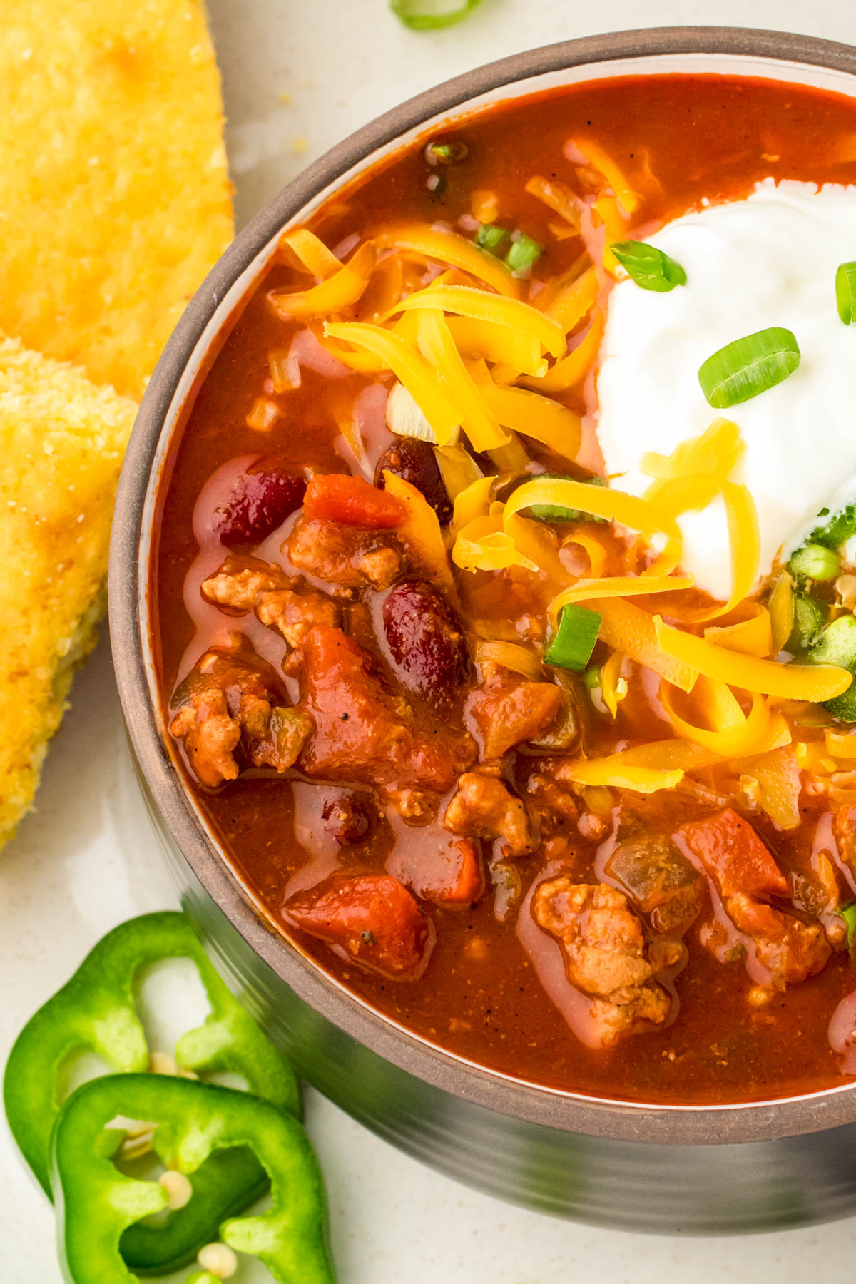 Close up of a black bowl filled with turkey chili and topped with cheddar cheese and sour cream.