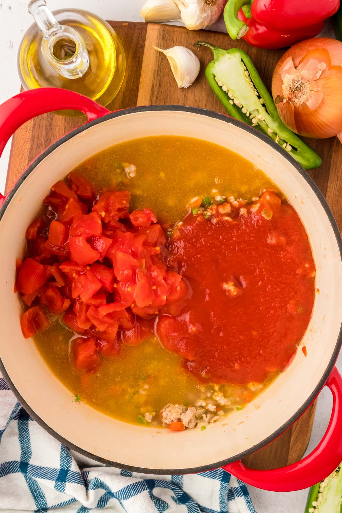 Tomato sauce and diced tomatoes being added to a Dutch oven with chicken stock, ground turkey, and veggies.