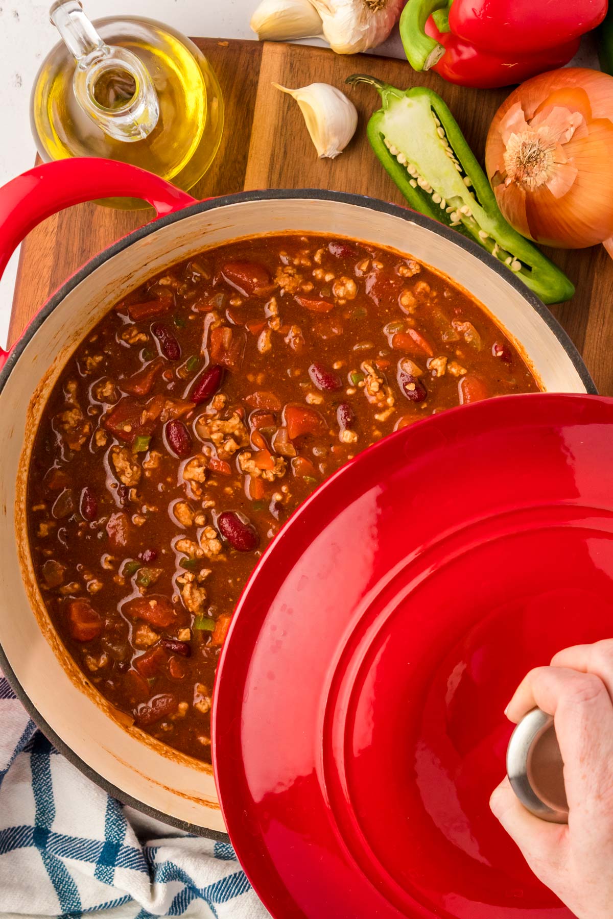 A woman's hand removing the lid of a red Dutch oven to reveal turkey chili inside.
