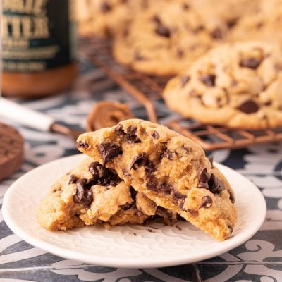 A cookie butter chocolate chip cookie broken in half on a white plate.