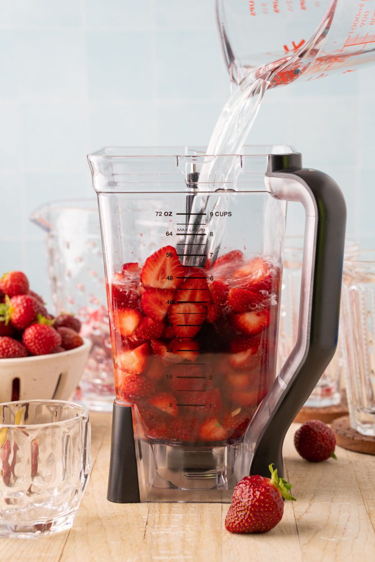 Water being added to a blender with strawberries, lemon juice, and simple syrup. 