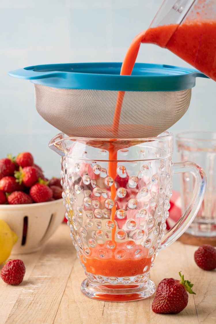 Strawberry puree being strained through a fine mesh sieve.