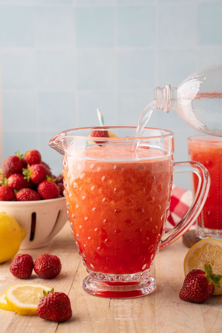 Club soda being poured into a pitcher of strawberry lemonade.