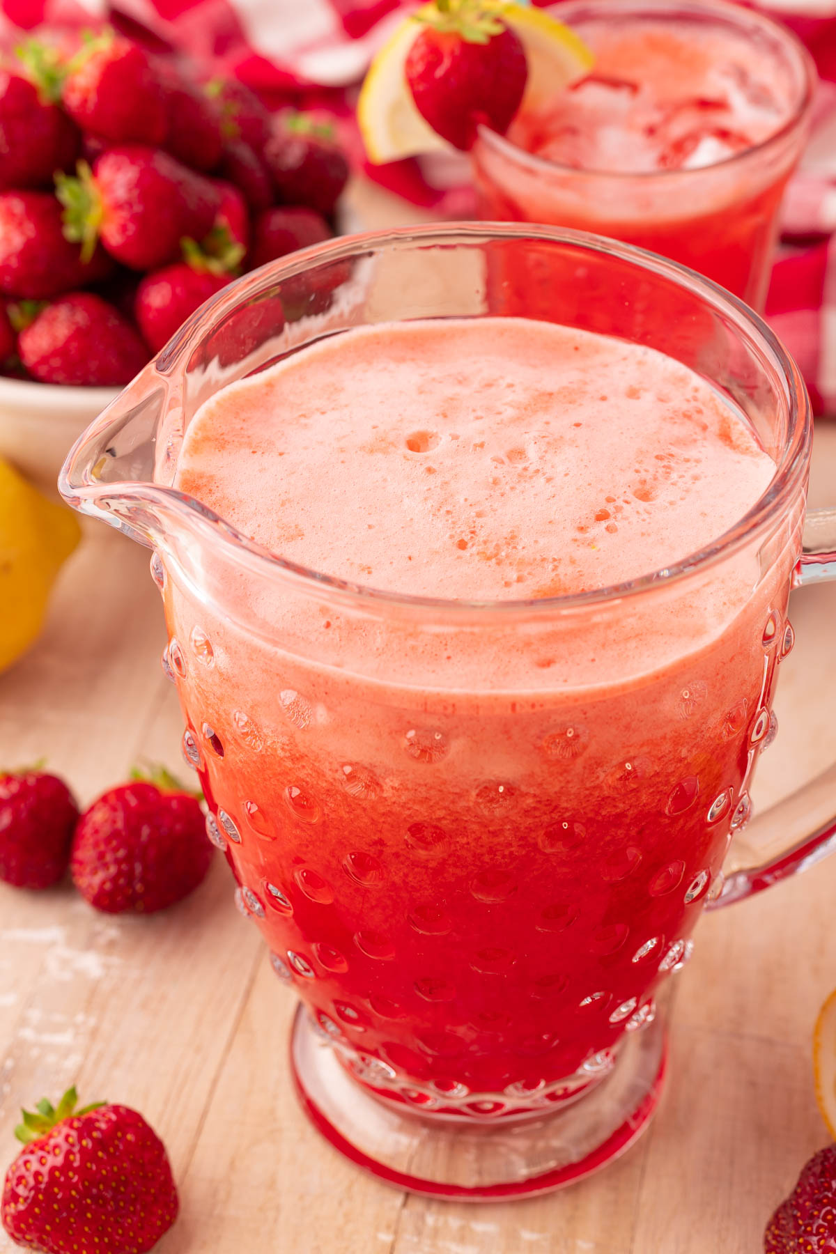 A pitcher of strawberry lemonade on a light wood table.