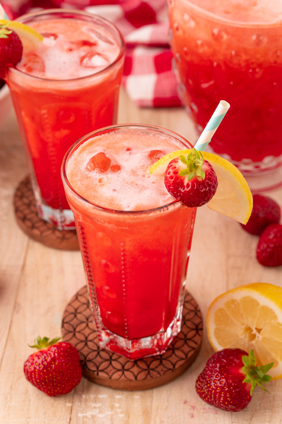 Glasses of strawberry lemonade on a wooden coaster on a table.