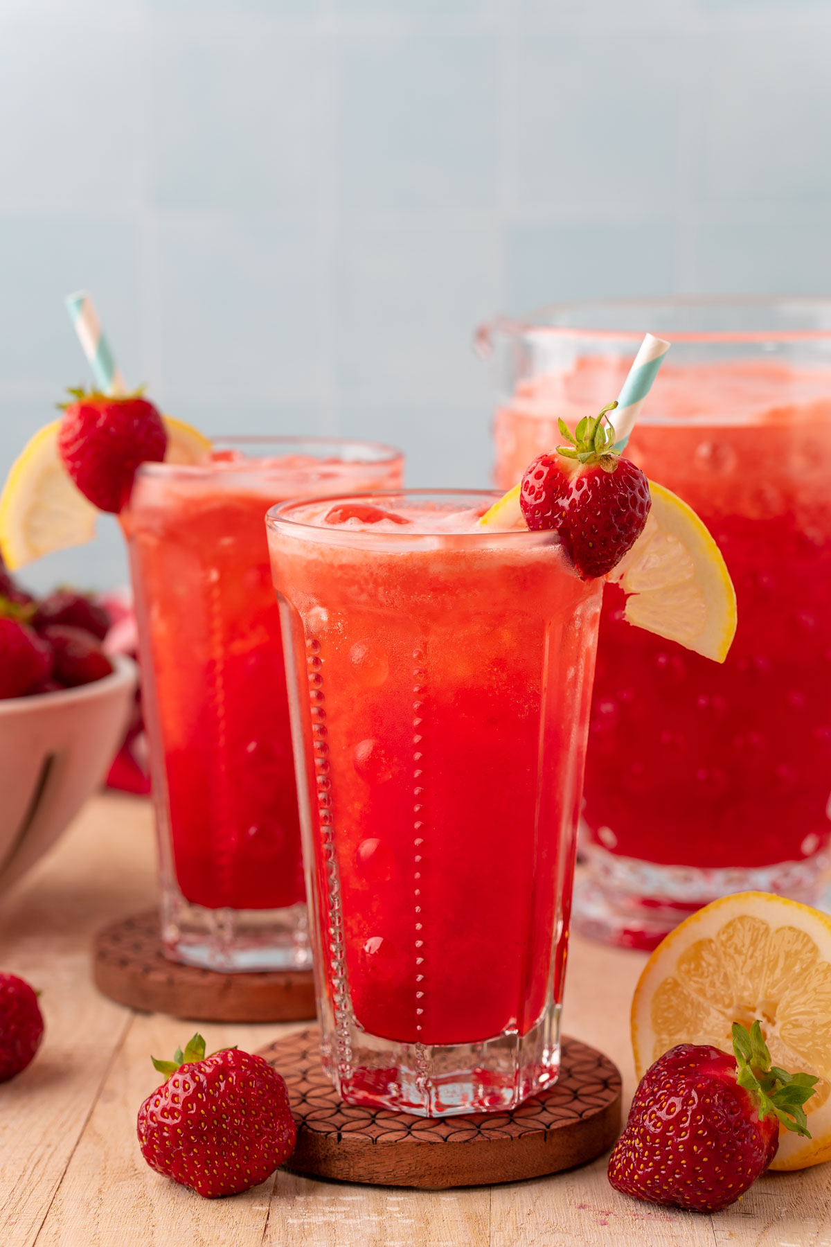 Two glasses of sparkling strawberry lemonade on wooden coasters.