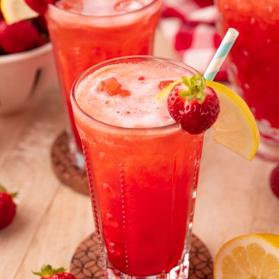 two glasses of strawberry lemonade on wooden coasters on a wooden table.