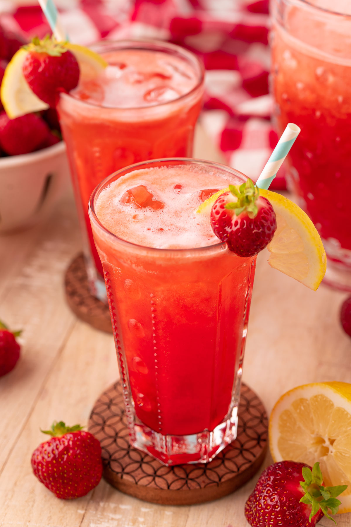 two glasses of strawberry lemonade on wooden coasters on a wooden table.