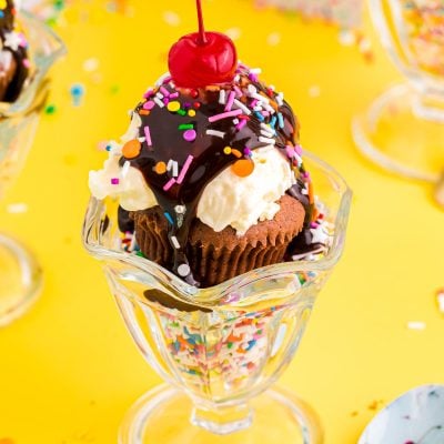 Close up photo of brownie cupcakes in a sundae dish filled with sprinkles on a yellow table.