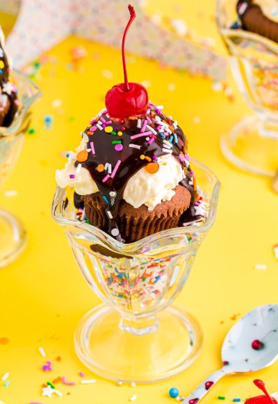 Close up photo of brownie cupcakes in a sundae dish filled with sprinkles on a yellow table.