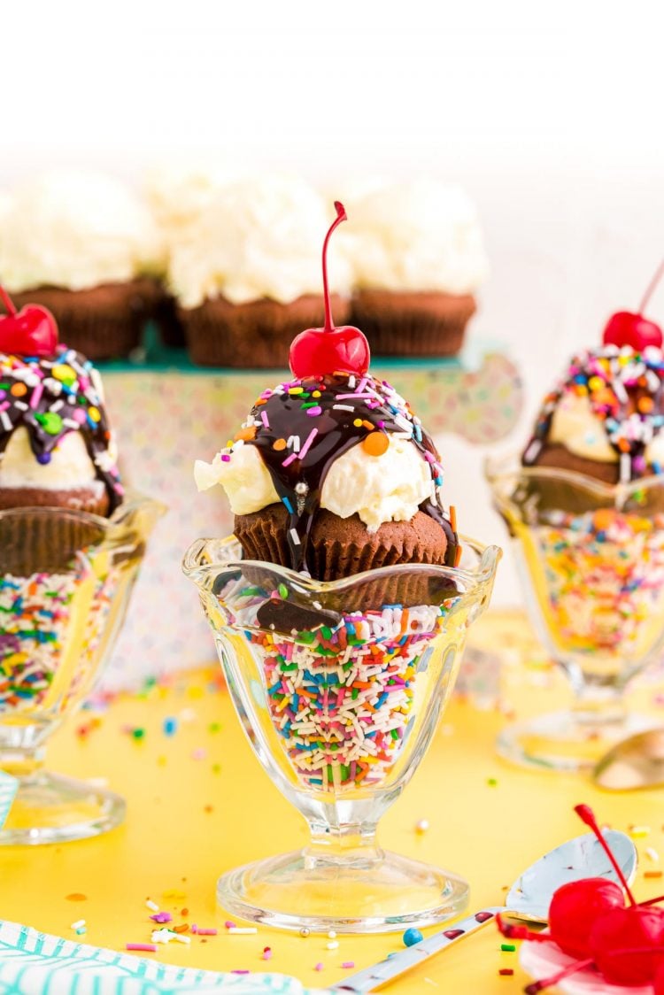 Straight on photo of brownie cupcakes in sundae dishes on a yellow surface.
