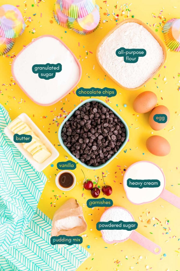 overhead photo of ingredients to make brownie cupcakes on a yellow surface with a teal napkin and rainbow sprinkles scattered around.