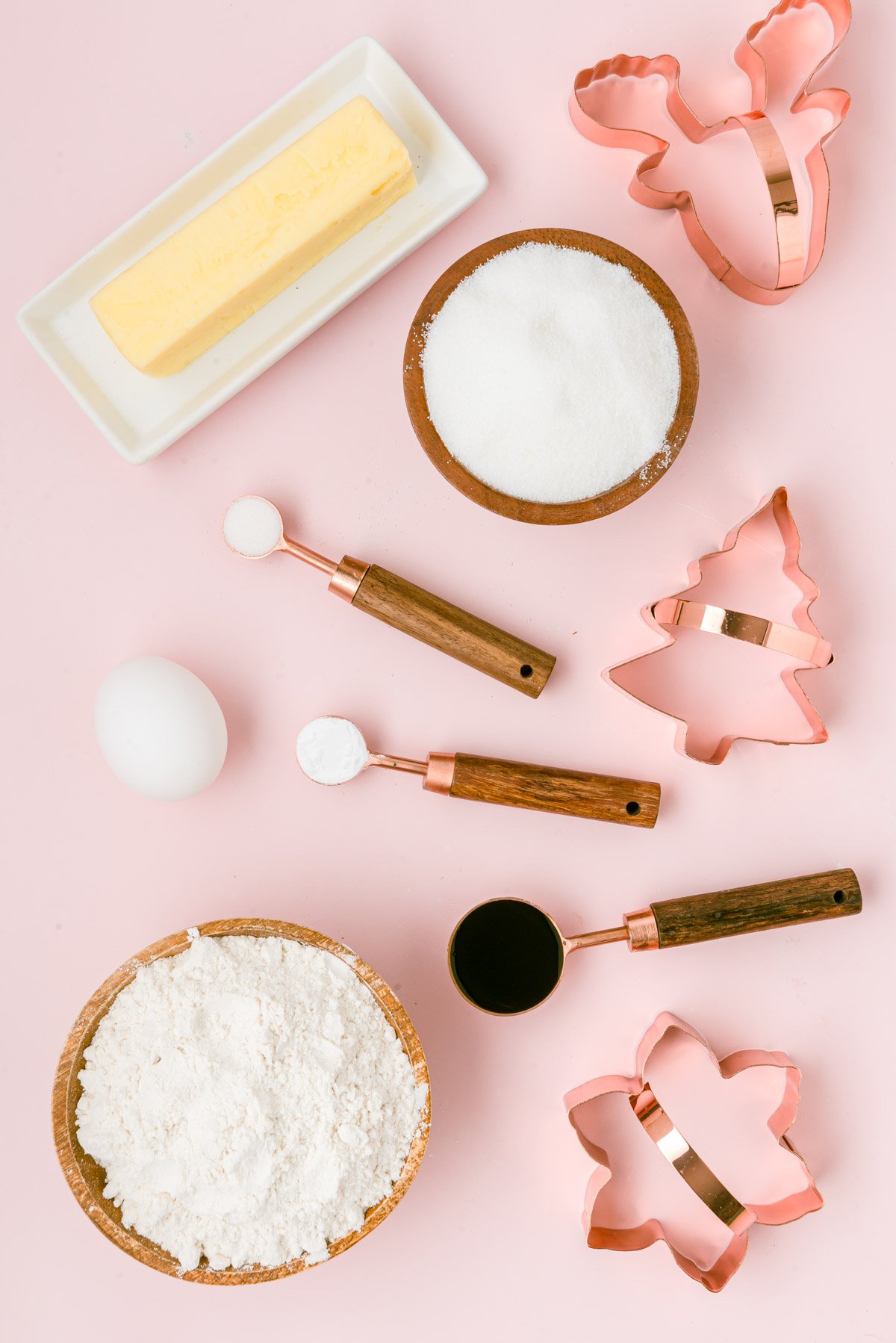 Ingredients to make cutout sugar cookies on a pink table.
