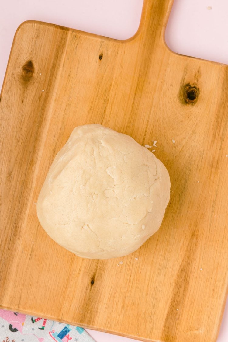 A ball of sugar cookie dough on a wooden board.