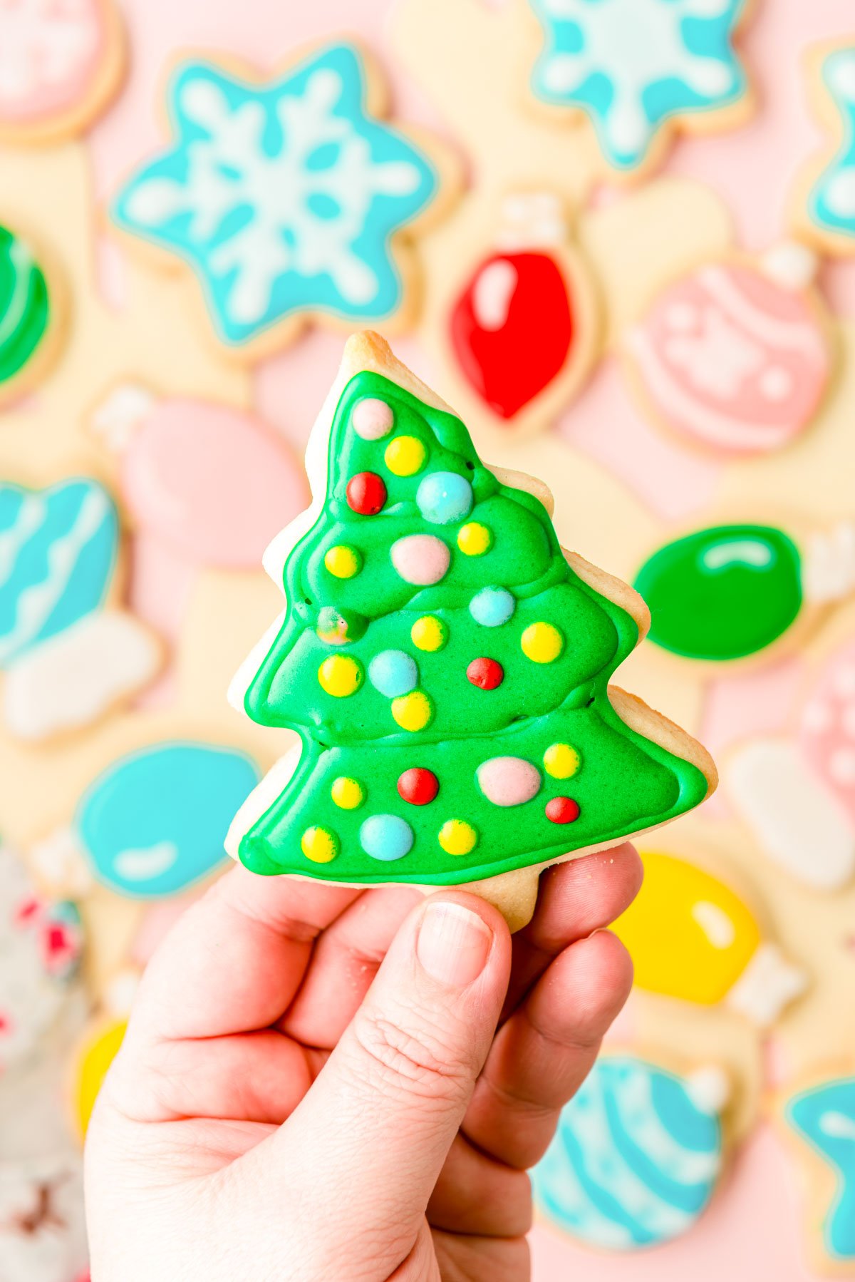 A woman's hand holing an iced Christmas tree cookie to the camera.