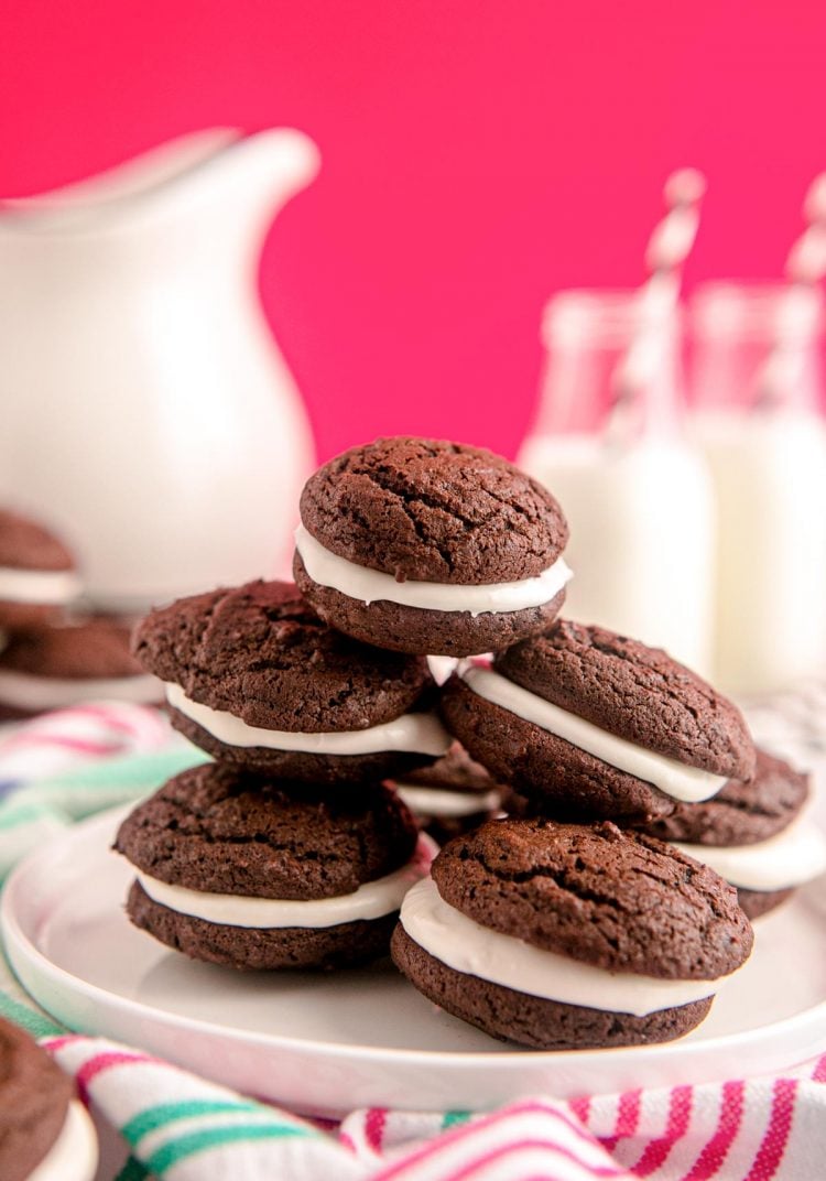 A white plate with whoopie pies on it with milk in the background.