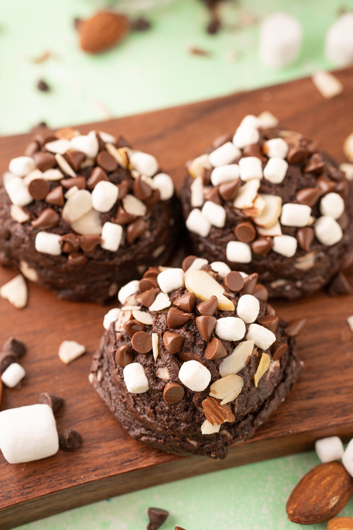 Three rocky road pudding cookies on a wooden serving board.