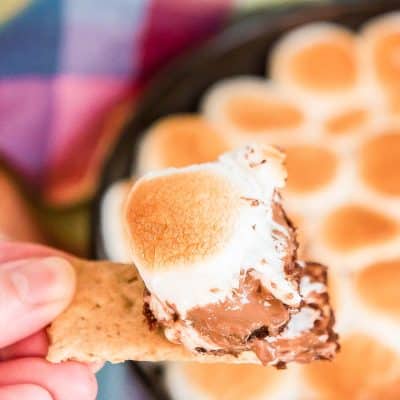 Woman's hand with a piece of graham cracker with a smores dip on it.