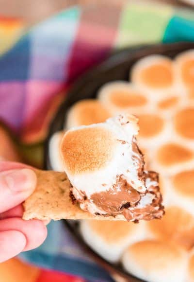 Woman's hand with a piece of graham cracker with a smores dip on it.