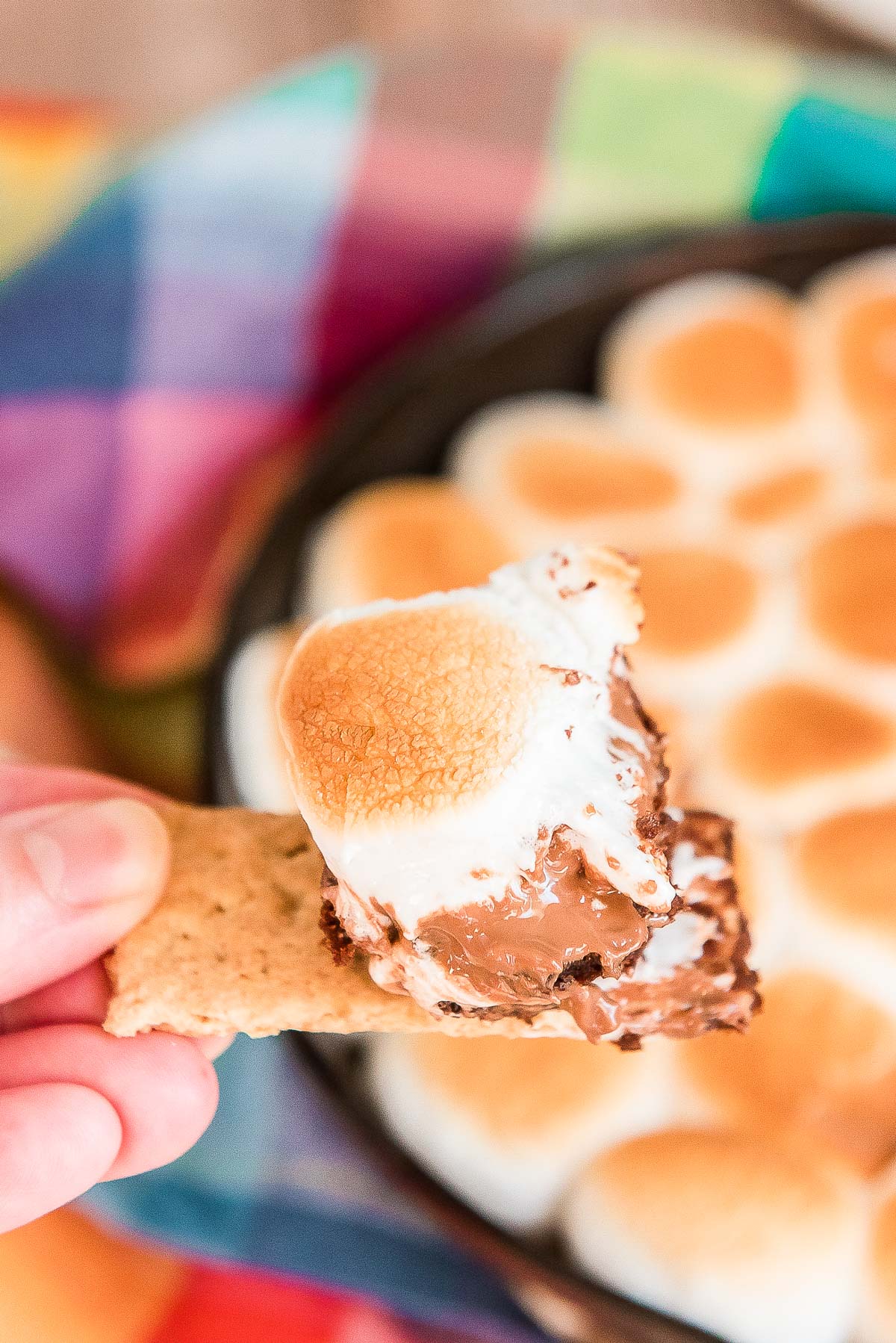 Woman's hand with a piece of graham cracker with a smores dip on it.