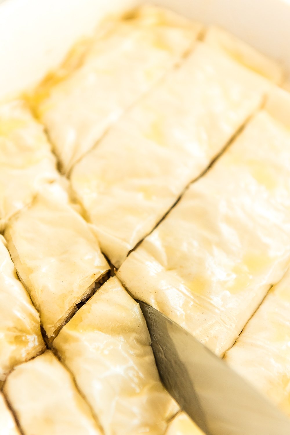 Baklava being cut with a large knife before going in the oven.