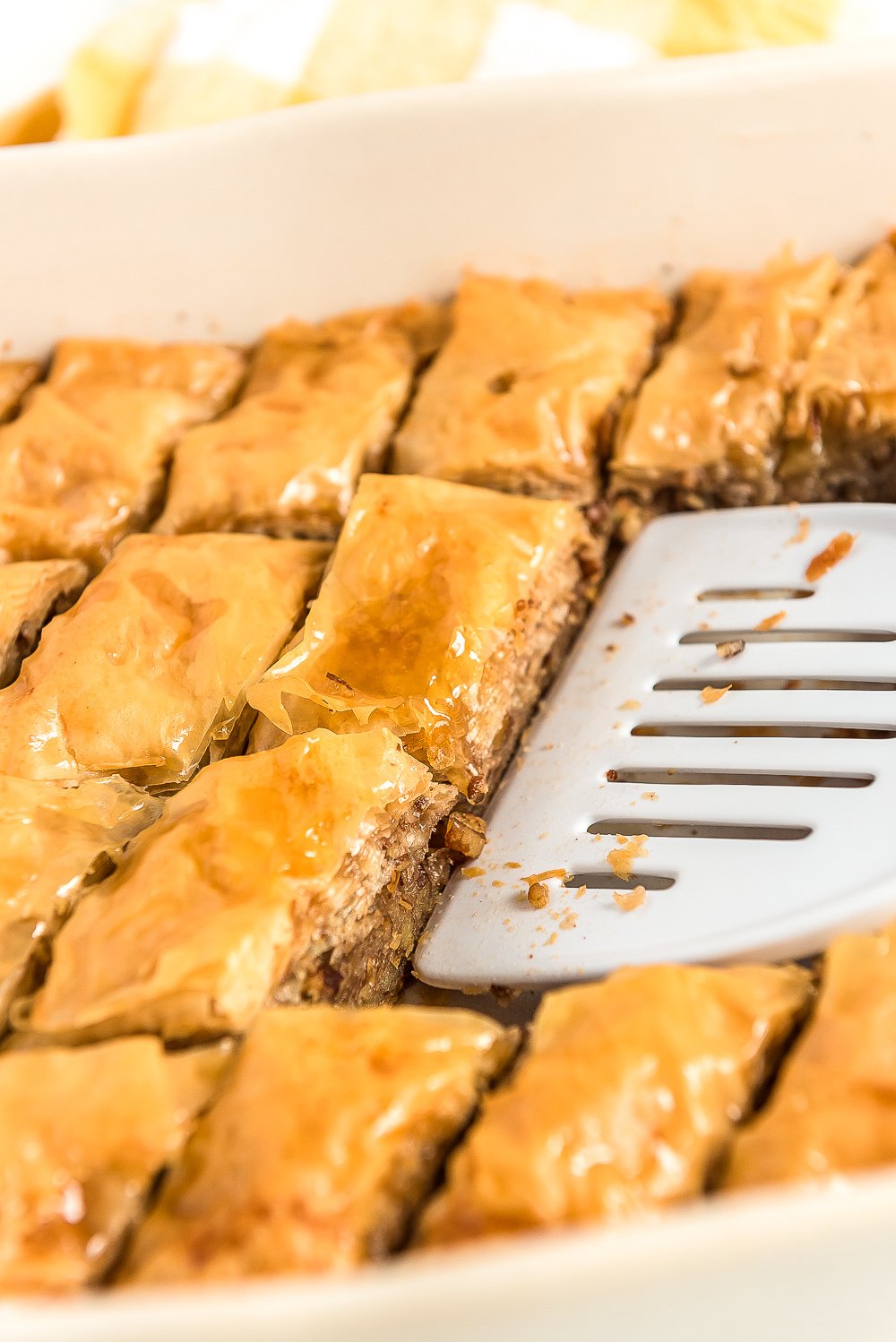 Spatula scooping pieces of baklava out of a baking dish.