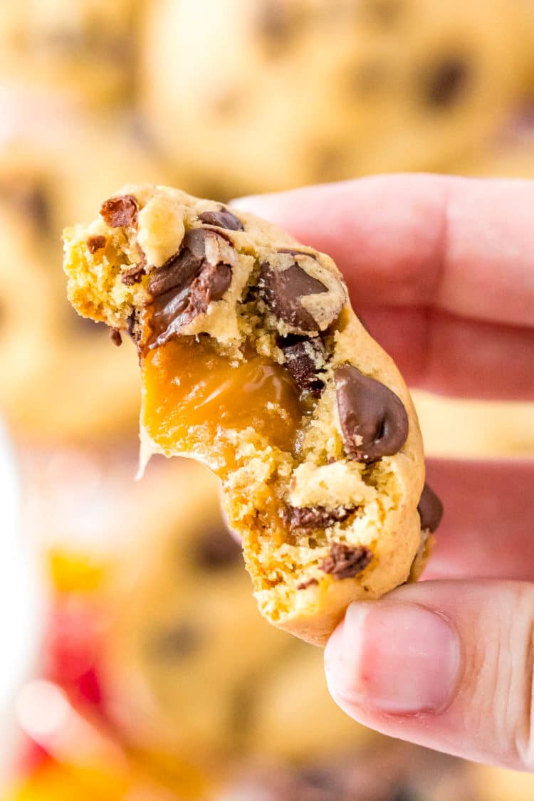 Close up photo of a chocolate chip cookie stuffed with a caramel candy with a bite taken out of it.