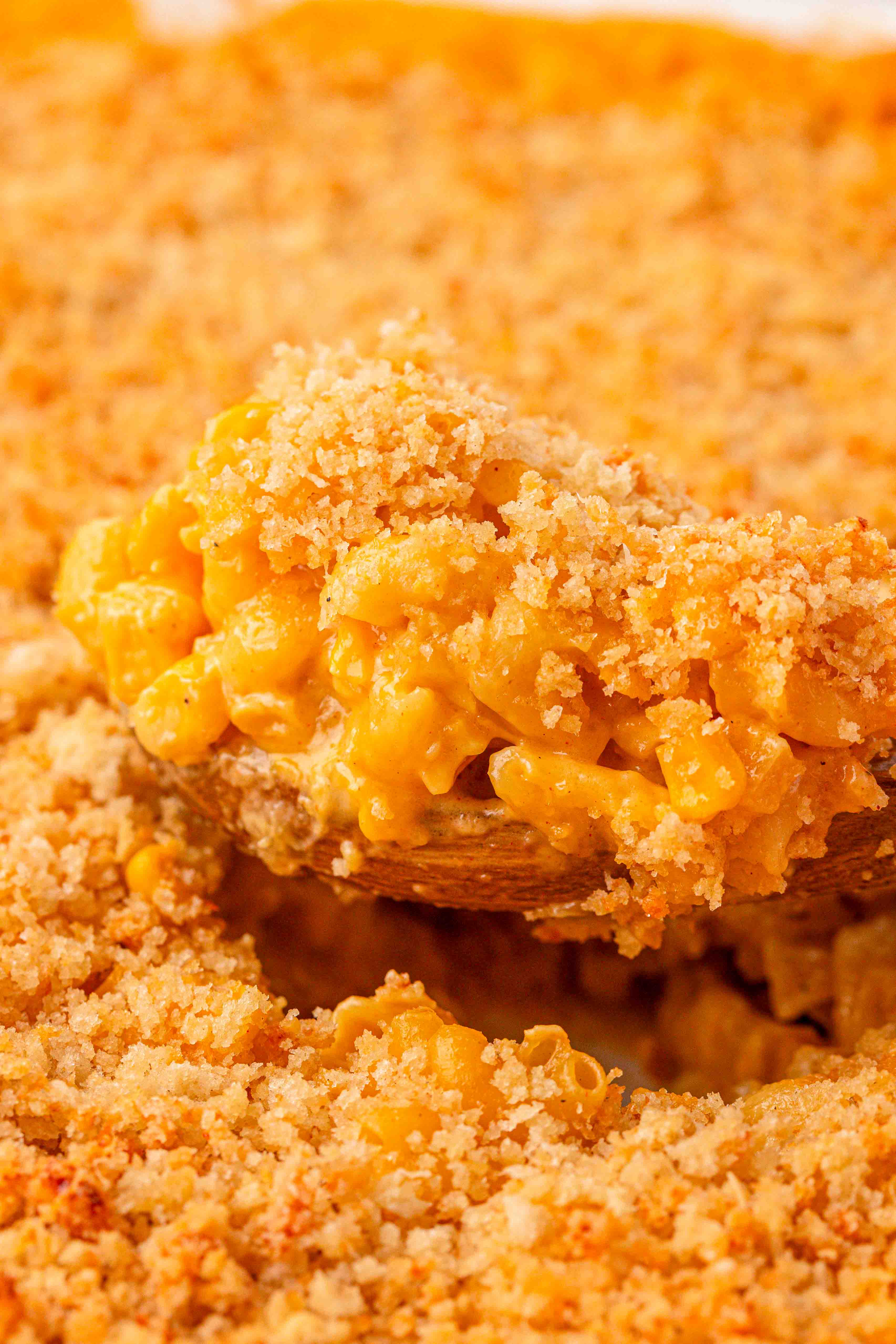 Close up of a spoon of corn mac and cheese being served from a baking dish.