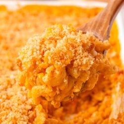 A wooden spoon of mac and cheese being lifted from a pan.