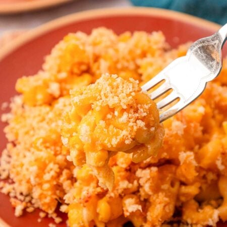 Corn mac and cheese on a red plate with a fork taking a bite.