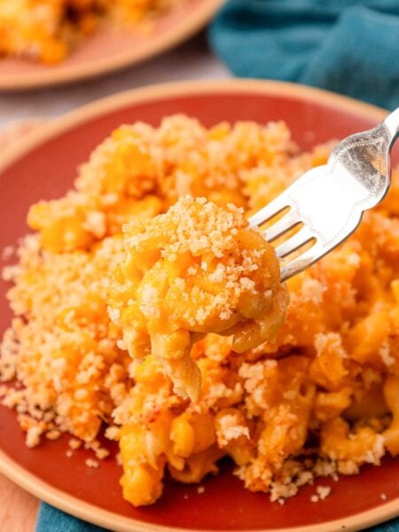 Corn mac and cheese on a red plate with a fork taking a bite.