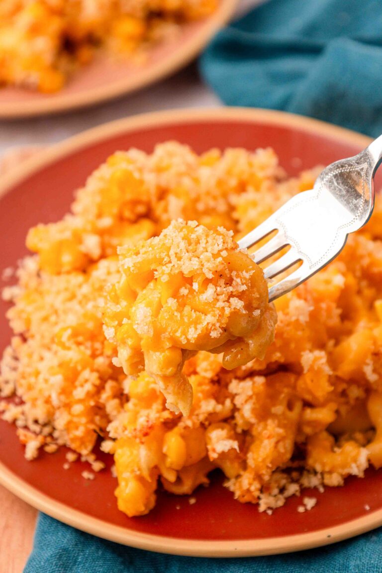 Corn mac and cheese on a red plate with a fork taking a bite.