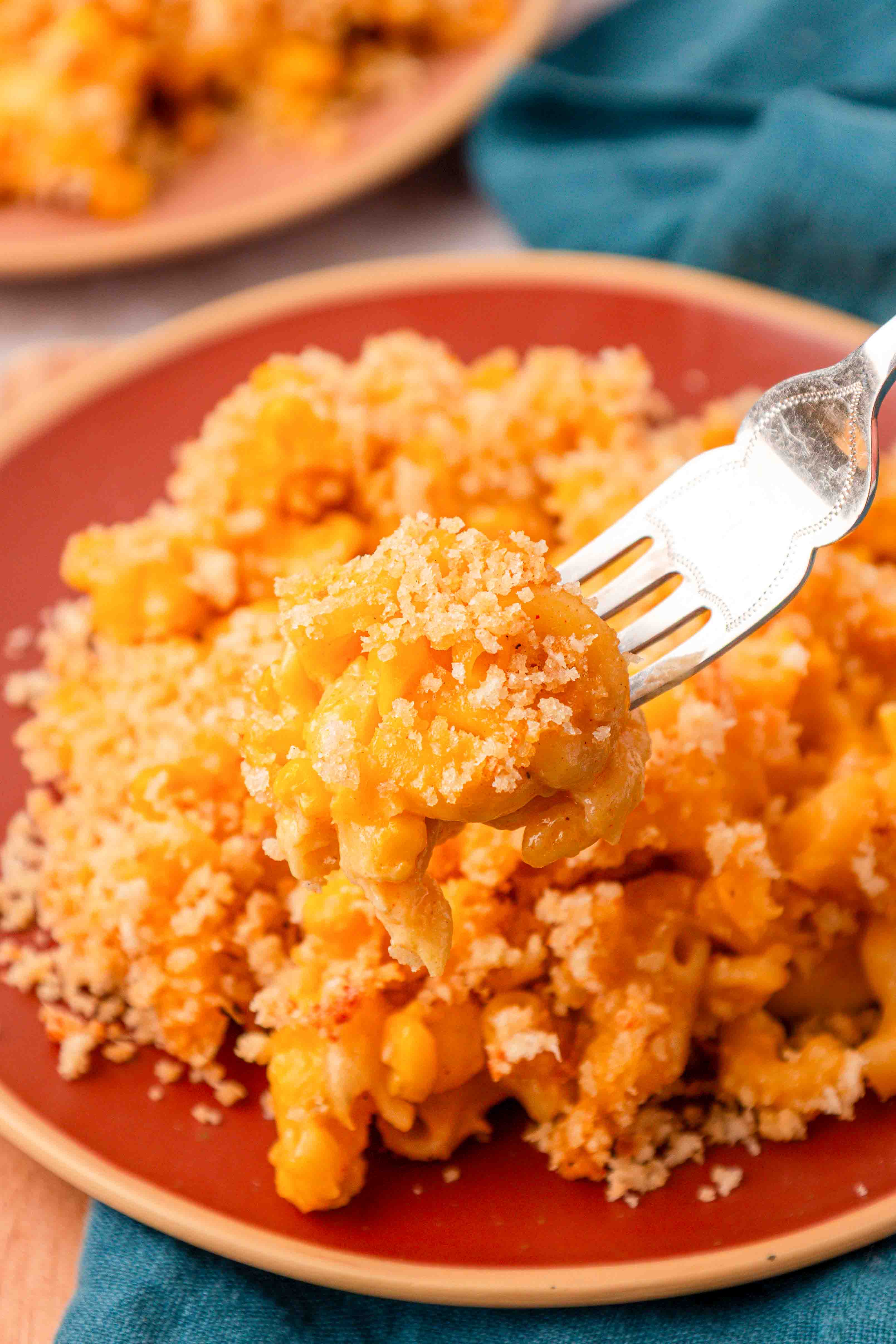 Corn mac and cheese on a red plate with a fork taking a bite.