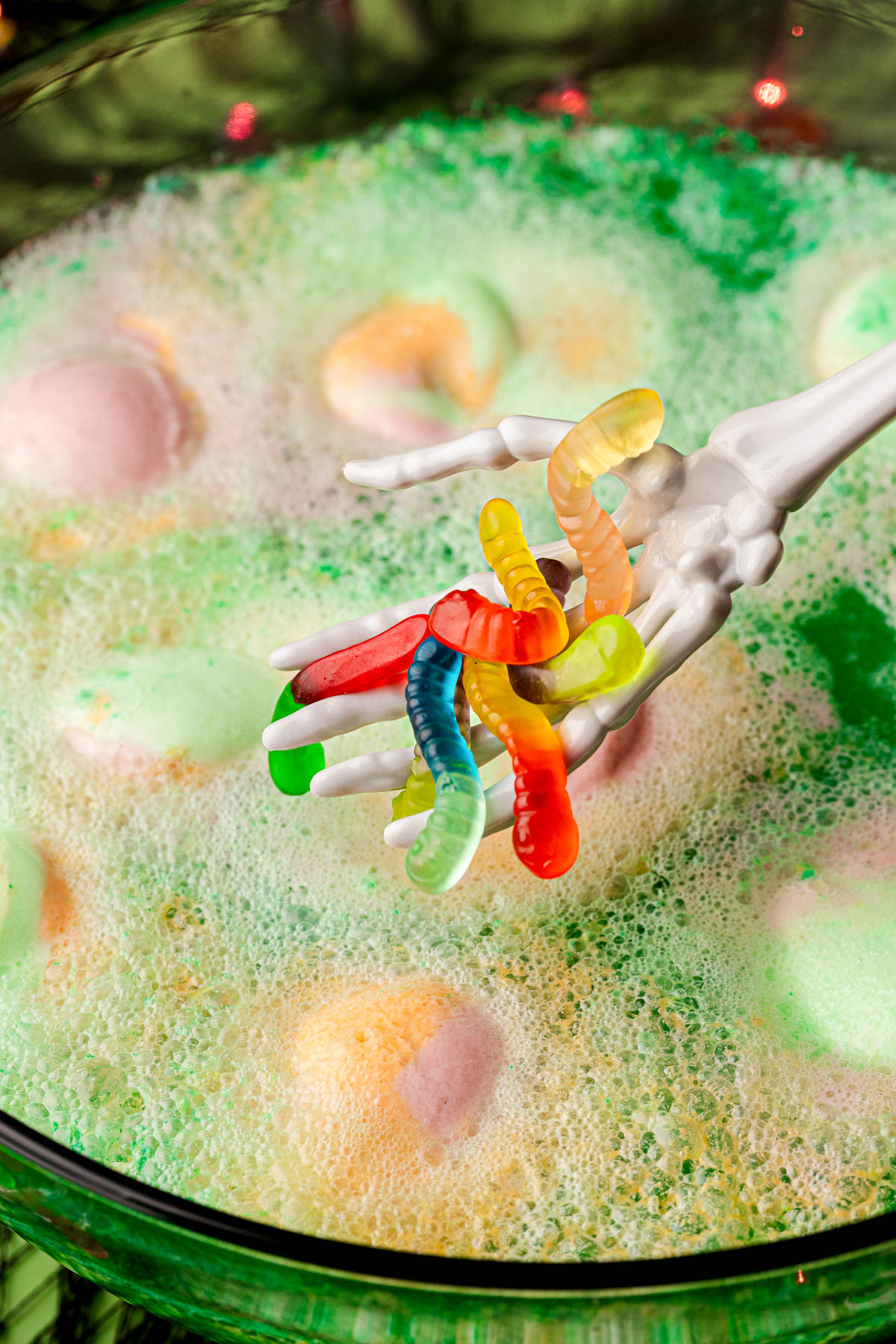 A plastic skeleton hand adding gummy worms to a bowl of Halloween punch.