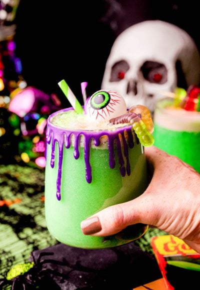 A woman's hand holding a cup of green Halloween party punch.