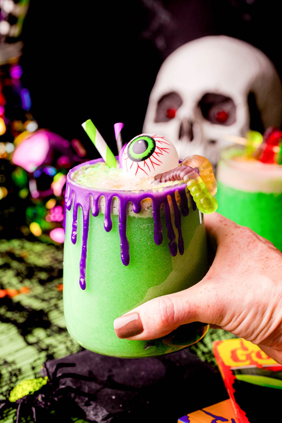 A woman's hand holding a cup of green Halloween party punch.