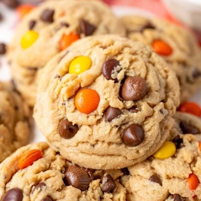 Close up of a peanut butter reese's pieces chocolate chip cookie on more cookies.