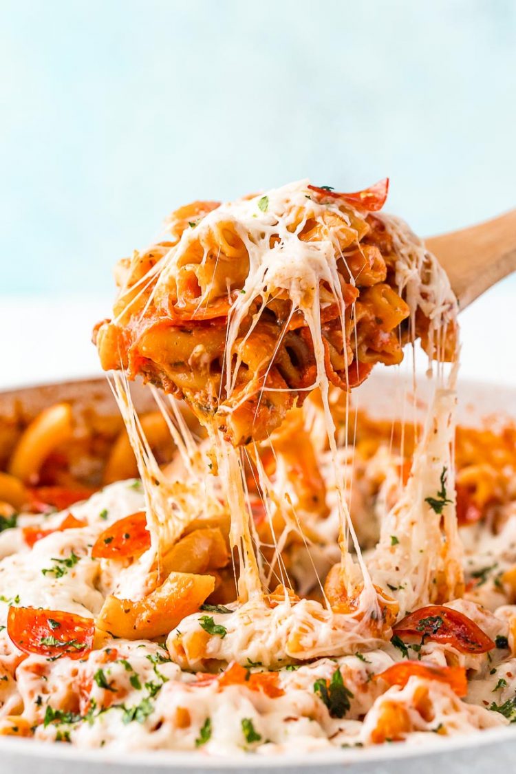 A scoop of pizza pasta being lifted from the pan. Cheese is stretching from the spoon to the pan.