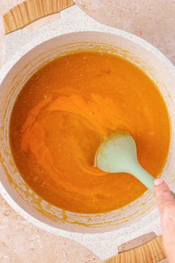 Eggs being mixed into a pot of melted butter and sugar.